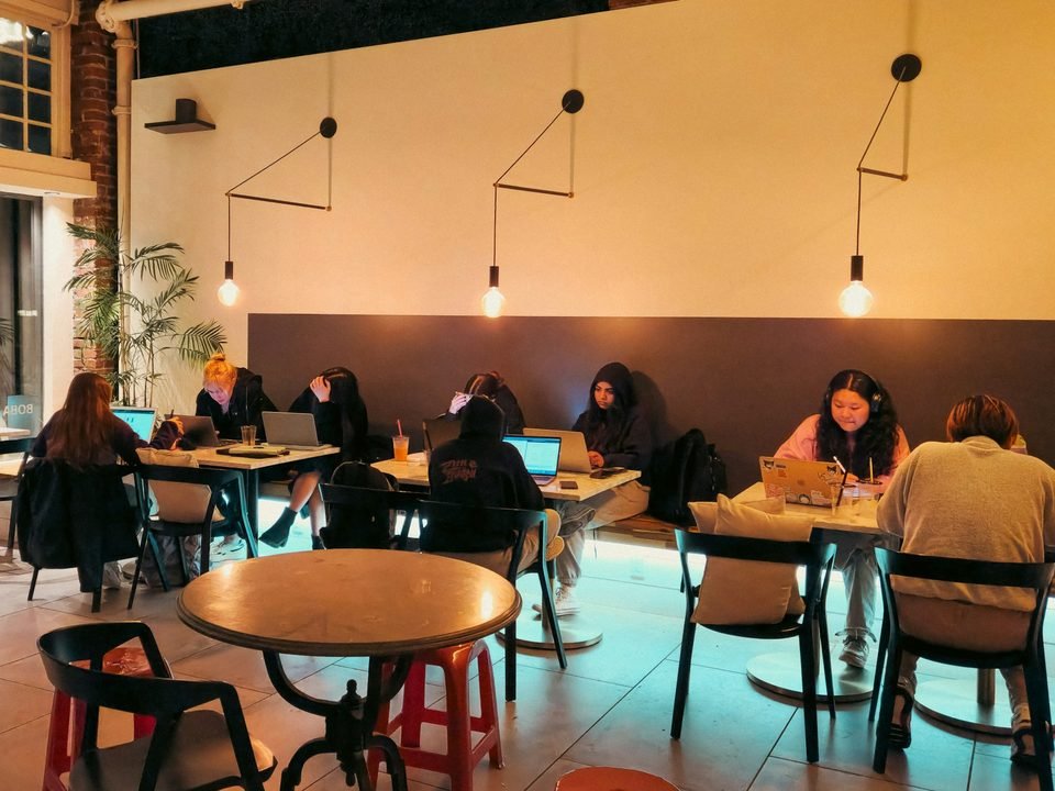 Lantai dua yang lebih tenang, orang bekerja dengan laptop di meja panjang